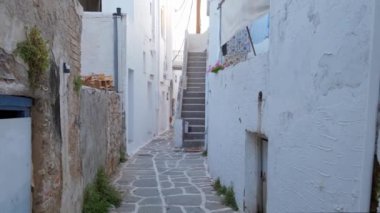 Yunanistan 'ın ünlü Paros Adası' ndaki Naousa kasabasının çiçek açan begonvil çiçekli geleneksel badanalı evleri ile pitoresk dar bir sokakta sabit kamerayla yürümek