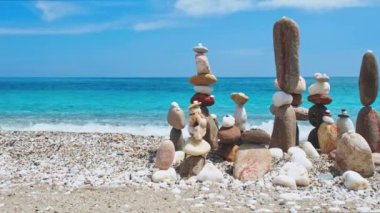 Denge ve uyum kavramı. Doğada mavi denizin sahil kıyısındaki çakıl taşı yığınları. Taş istifleme meditasyon sanatı. Kamera yatay doli takip ediyor. Agia Kiriaki plajı, Milos adası, Yunanistan