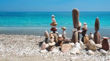Denge ve uyum kavramı. Doğada mavi denizin sahil kıyısında çakıl taşları yığılıyor. Taş istifleme meditasyon sanatı. Kamera yatay kule takibi