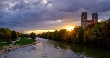 Münih 'in dramatik günbatımında geçen zamanı: Bavyera' nın ünlü turistik kentinde sonbahar. Reichenbach Köprüsü 'nden Isar nehri, ağaçlar ve kilise manzarası. Munchen, Bavyera, Almanya.
