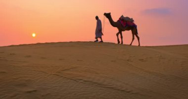 Gün batımında Thar Çölü 'nün kum tepelerinde deve ile bedevi süren Hint kamelecisi. Rajasthan seyahat turizmi arka plan safari macerası. Jaisalmer, Rajasthan, Hindistan