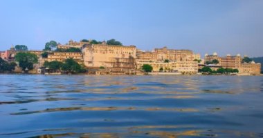 Günbatımında Udaipur Şehir Sarayı 'nın bulutlu gökyüzü ve turist teknesi yüzey manzaralı ünlü Rajasthan turistik merkezi manzarası. Udaipur, Rajasthan, Hindistan