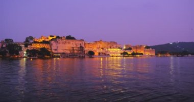 Pichola Gölü kıyısındaki ünlü lüks Udaipur Sarayı, gün batımında su dalgalarıyla aydınlandı. Mewar Hanedanı 'nın Rajput mimarisi. Udaipur, Rajasthan, Hindistan.