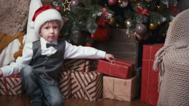 Noel Baba şapkalı küçük mutlu çocuk Noel ağacının altında hediyeleri kontrol ediyor. Noel arifesinde çocuk hediye kutusunu açıyor. Noel konsepti