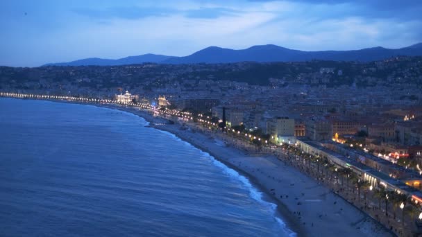 ニース フランスの夜の青の時間の風景です 地中海の波が海岸で急増し 人々はビーチでリラックスし カラフルな家の照明 — ストック動画