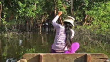 KAMPONG PHLUK, CAMBODIA - 21 ARALIK 2013: Su basmış ağaçlarla dolu mangrov yağmur ormanlarında yüzen sandalda kürek çeken kadın