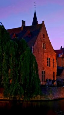 Bruges turistik merkezinin ünlü manzarası - Belfry ile Rozenhoedkaai kanalı ve geceleri ağaçlı kanal boyunca eski evler. Brugge, Belçika. Kamera tavası