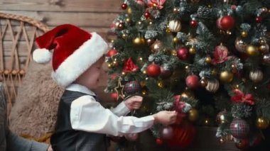 Noel Baba şapkalı küçük bir çocuk noel ağacını süsleyerek süslüyor.