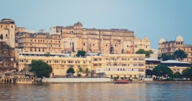 Günbatımında Pichola Gölü 'nden Udaipur Şehir Sarayı manzaralı bir turist teknesi geçiyor. Jag Niwas Rajput mimarisinin bir örneğidir. Rajasthan, Hindistan 'ın popüler turistik yeridir. İnanılmaz Hindistan mirası..