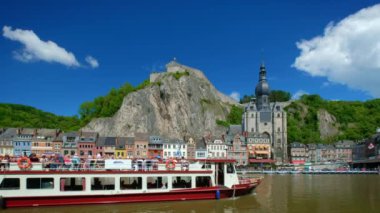 DINANT, BELIGUM - 30 Mayıs 2018: Meuse nehrinin üzerinde turist botuyla Dinant şehri manzarası. Dinant, Belçika 'nın Namur ilinin Meuse Nehri üzerinde yer alan bir Walloon şehridir..
