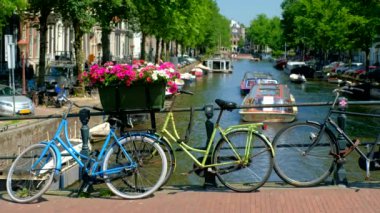 AMSTERDAM, NETHERLANDS - 21 Mayıs 2018: Amsterdam Kanalı 'nda geçen botlar, çiçekler ve bisikletli köprü. Amsterdam, Hollanda