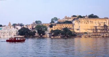 Udaipur, Hindistan - 11 Kasım 2019: Pichola Gölü, Şehir Sarayı ve Jag Niwas Sarayı Rajput mimarisinde turist teknesi. Rajasthan, Hindistan 'ın popüler turizm merkezidir. Kamera tekneyi takip ediyor.