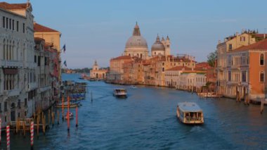 Venedik, İtalya - 19 Temmuz 2019 'da Venedik Büyük Kanalı' nın gün batımında Ponte dell 'Accademia Köprüsü' nden Santa Maria della Salute Kilisesi 'ne giden gondol ve vaporetto tekneli görüntüsü