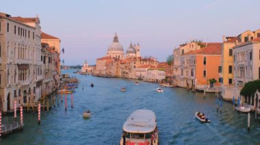 Venedik, İtalya - 19 Temmuz 2019 'da Venedik Büyük Kanalı' nın gün batımında Ponte dell 'Accademia Köprüsü' nden Santa Maria della Salute Kilisesi 'ne giden gondol ve vaporetto tekneli görüntüsü