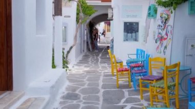NAOUSA, GREECE - 19 Mayıs 2019: Yunanistan 'ın Paros Adası' nın ünlü turistik beldesi Paros 'ta, Naousa kasabasının çiçek açan begonvil çiçekli, badanalı evleri ile pitoresk caddede sabit bir kamerayla yürümek