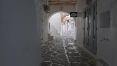 NAOUSA, GREECE - 27 Mayıs 2019: Yunanistan 'ın Paros Adası' nın ünlü turistik beldesi Paros 'ta, Naousa kasabasının çiçek açan begonvil çiçekli, badanalı evleri ile pitoresk caddede sabit bir kamerayla yürümek