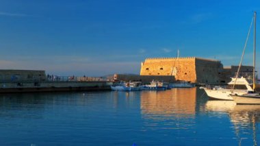 HERAKLION, GREECE - 18 Mayıs 2019: Heraklion 'daki Venedik kalesi ve günbatımında Yunanistan' ın Girit Adası 'ndaki balıkçı tekneleri. Yatay kamera tavası