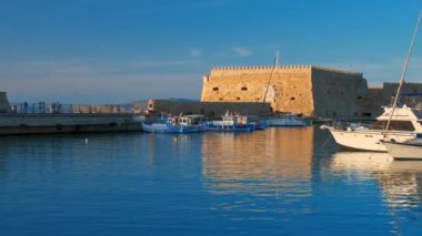 HERAKLION, GREECE - 18 Mayıs 2019: Heraklion 'daki Venedik kalesi ve günbatımında demirli balıkçı tekneleri, Girit Adası, Yunanistan. Yatay kamera tavası