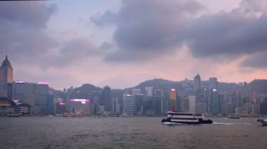 Hong Kong, Çin - 28 Nisan 2018: Hong Kong şehir merkezi gökdelenleri Victoria Limanı üzerinde akşamları turist botu ve feribot ile birlikte. Kamera arkası feribotu takip ediyor