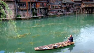 FENGHUANG, ÇİN - 25 Nisan 2018: Feng Huang Antik Kenti 'nde (Phoenix Antik Kenti), Tuo Jiang Nehri' nde, köprüsü ve turist teknesi olan tanımlanamayan Çinli adam. Hunan Eyaleti, Çin