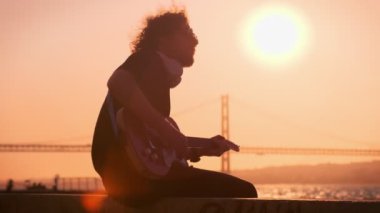 Günbatımında sokakta elektro gitar çalan siyahlı hippi sokak müzisyeni.