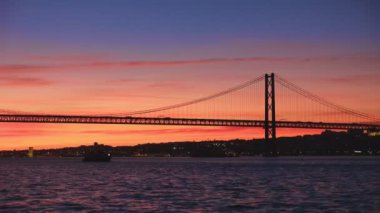 25 de Abril Köprüsü 'nün Tagus nehri üzerinde Setubal Yarımadası' nda Lisboa ve Almada 'yı gün batımında turist yatı silüetiyle birbirine bağlayan ünlü turistik manzarası. Lizbon, Portekiz