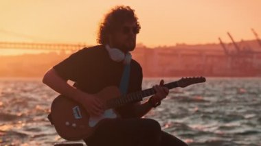 Günbatımında sokakta elektro gitar çalan siyahlı hippi sokak müzisyeni.