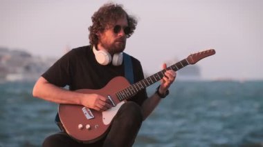 Hipster sokak müzisyeni, günbatımında sette elektro gitar çalıyor.