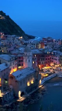 Cinque Terre Ulusal Parkı 'ndaki Vernazza köyünde kayalıklarda bulunan popüler turizm merkezleri akşam saatlerinde aydınlanan UNESCO Dünya Mirasları Sitesi, Vernazza, Liguria, İtalya. Kamera kaydıyla