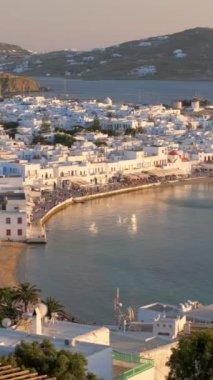 Ünlü yel değirmenleriyle Mykonos kasabası manzarası ve yaz günbatımında tekne ve yatlarla liman manzarası. Mykonos, Cyclades adaları, Yunanistan. Kamera kaydıyla