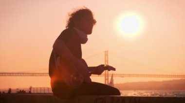 Günbatımında sokakta elektro gitar çalan siyahlı hippi sokak müzisyeni.