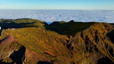 Pico 'nun hava görüntüsü, dağların askeri radarıyla gün batımında çiçek açan Cytisus çalılarıyla Arieiro' yu gösteriyor. Madeira Adası, Portekiz. Çekim