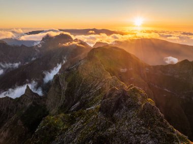 Gün batımında Pico Ruivo yakınlarında bulutların üzerindeki dağların insansız hava aracı görüntüsü. Madeira Adası, Portekiz