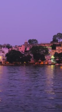 Ünlü lüks Udaipur Şehir Sarayı, Lal ghat, Pichola Gölü kıyısında evler günbatımında su dalgalarıyla aydınlandı - Mewars 'ın Rajput mimarisi. Udaipur, Rajasthan, Hindistan. Yatay tava