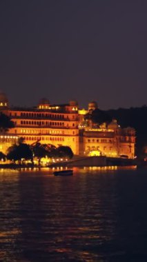 Ünlü lüks Udaipur Şehir Sarayı ve Pichola Gölü 'ndeki Jag Niwas Gölü Sarayı günbatımında su dalgalarıyla aydınlandı. Mewar Hanedanı hükümdarlarının Rajput mimarisi. Udaipur, Rajasthan, Hindistan.