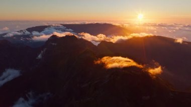 Pico Ruivo 'da gün batımında bulutlu dağların uçuş görüntüsü. Madeira Adası, Portekiz. Geri çekilin. Doli atış.