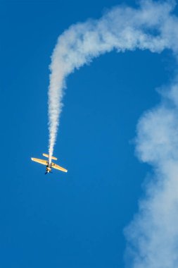 Altın dublör akrobatik uçak mavi gökyüzünde dumanla gösteri yapıyor. Hız kavramı, zorluk, kesinlik, risk