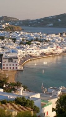 Ünlü yel değirmenleriyle Mykonos kasabası manzarası ve yaz günbatımında tekne ve yatlarla liman manzarası. Mykonos, Cyclades adaları, Yunanistan. Kamera kaydıyla