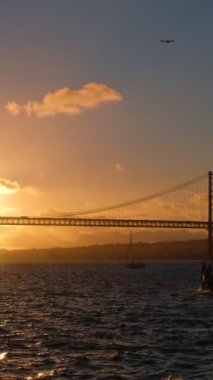 25 de Abril Köprüsü 'nün Lizbon' un ünlü turistik beldesi Setubal Yarımadası 'ndaki Lisboa ve Almada' yı Tagus Nehri üzerinde günbatımında yat silueti ve uçan uçakla birbirine bağlıyor. Lizbon, Portekiz