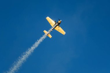 Altın dublör akrobatik uçak mavi gökyüzünde dumanla gösteri yapıyor. Hız kavramı, zorluk, kesinlik, risk