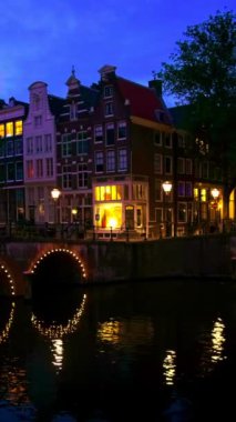 Amsterdam cityscape kanal, köprü ve ışıklı akşam alacakaranlık Ortaçağ evleri ile gece manzarası. Amsterdam, Hollanda