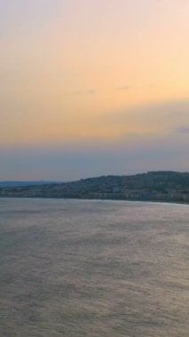 Nice, Fransa 'nın gün batımındaki manzarası. Akdeniz dalgaları sahilde dalgalanır, insanlar sahilde dinlenir, arabalar yolda ilerler. Güzel, France. Kamera yatay tavası