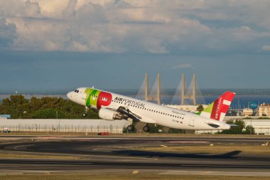 Lisbon, Portugal - September 11, 2023: TAP Air Portugal Airbus A320-214 passenger plane take off in Humberto Delgado Airport in Lisbon on sunset with Vasco da Gamma bridge in background clipart