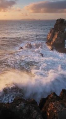 Cabo Carvoeiro, Peniche, Portekiz 'de günbatımında okyanus kıyısındaki kayalık dalgalarla çarpışıyor.