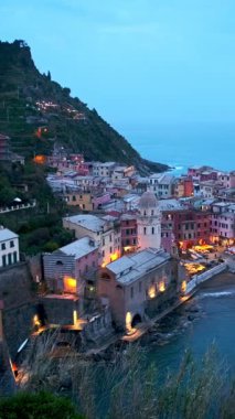 Cinque Terre Ulusal Parkı 'ndaki Vernazza köyünde kayalıklarda bulunan popüler turizm merkezleri akşam saatlerinde aydınlanan UNESCO Dünya Mirasları Sitesi, Vernazza, Liguria, İtalya. Kamera kaydıyla