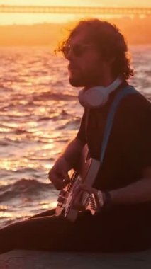 Günbatımında sokakta elektro gitar çalan siyahlı hippi sokak müzisyeni.