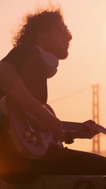 Günbatımında sokakta elektro gitar çalan siyahlı hippi sokak müzisyeni.