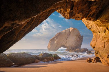 Penedo do do Guincho, Portekiz Praia da Santa Cruz 'da büyük bir kaya kemeri. Okyanus dalgaları ve gün batımında mağaradan görünen kumlu plajlar.