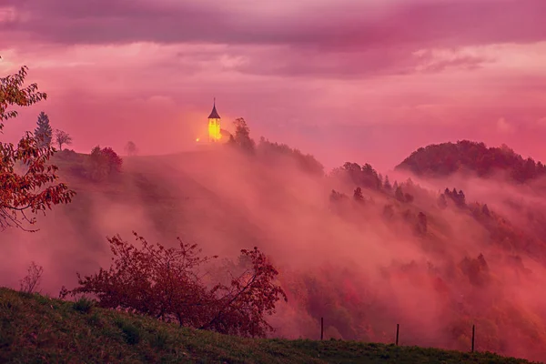 霧の丘 ピンクの空とスロベニアの教会ジャミニクの美しい日の風景 — ストック写真