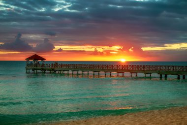 Dominik Cumhuriyeti 'ndeki güzel Karayip plajı. Mavi deniz suyu, renkli gökyüzü ve ahşap iskele ile tropikal cennet manzarası.